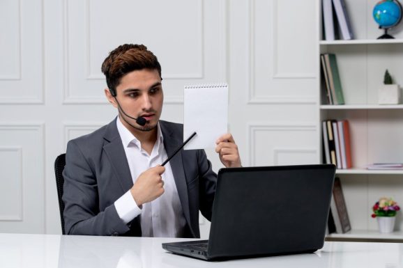 customer-service-young-cute-guy-grey-office-suit-with-computer-showing-notes-paper-min
